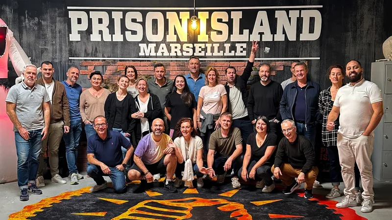 Une trentaine de personnes posent en deux rangs devant l'enseigne Prison Island Marseille, l'emblème peint au sol